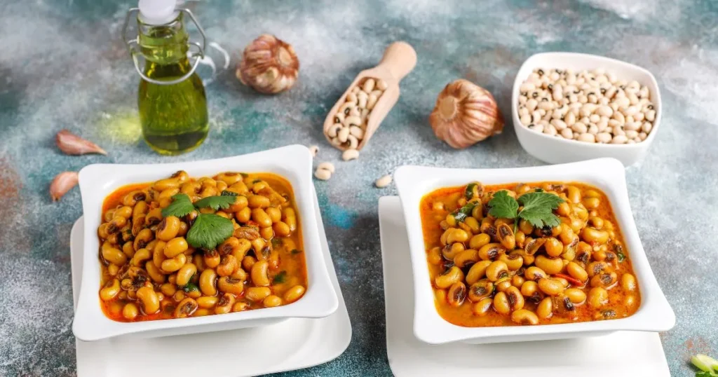 A plate of baked beans mixed with ground hamburger meat, garnished with fresh parsley, served with toasted bread. A bowl of fries is blurred in the background.